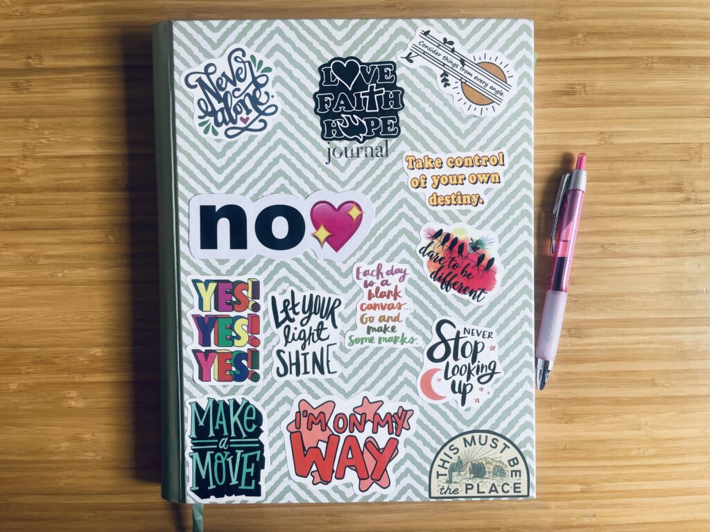 A journal decorated with colorful motivational stickers and a pink pen, representing faith, self-reflection, and intentional growth.