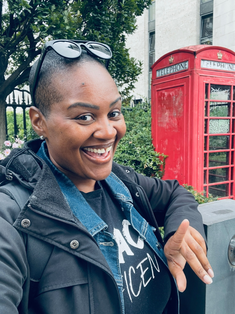 Joval, a Black woman, laughing joyfully in front of a iconic red London telephone box